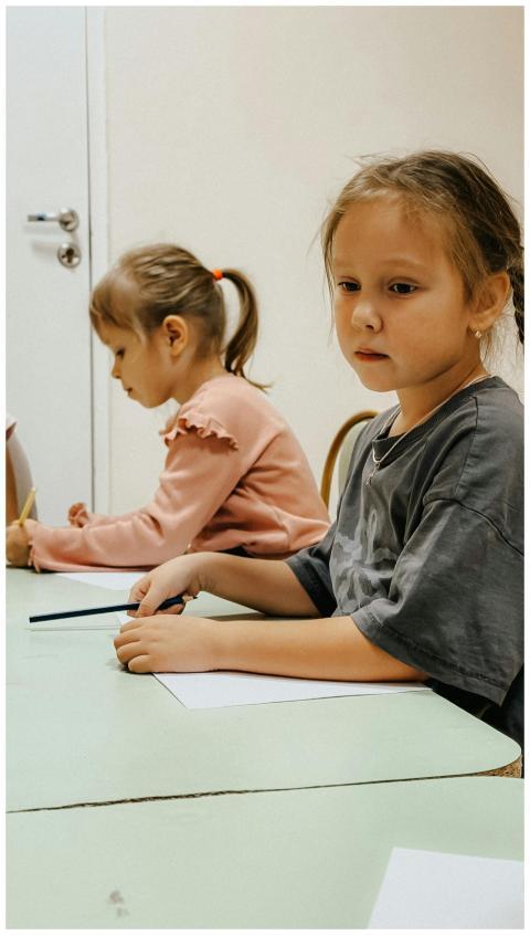 Two young girls sitting at a table, focused on dra