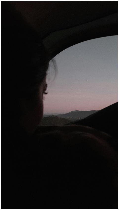 A woman watches a serene sunset from a car, captur