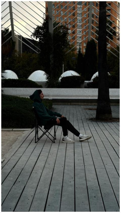 Young adult in a hoodie seated in a city park with