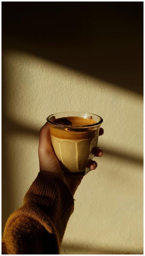 A cozy hand holding a coffee glass in a sunlit roo