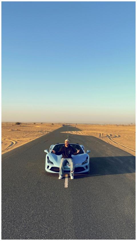 A man sits on a luxury sports car parked on a dese