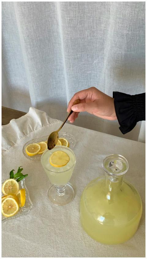 Lemonade in a glass with sliced lemon, jug, and a