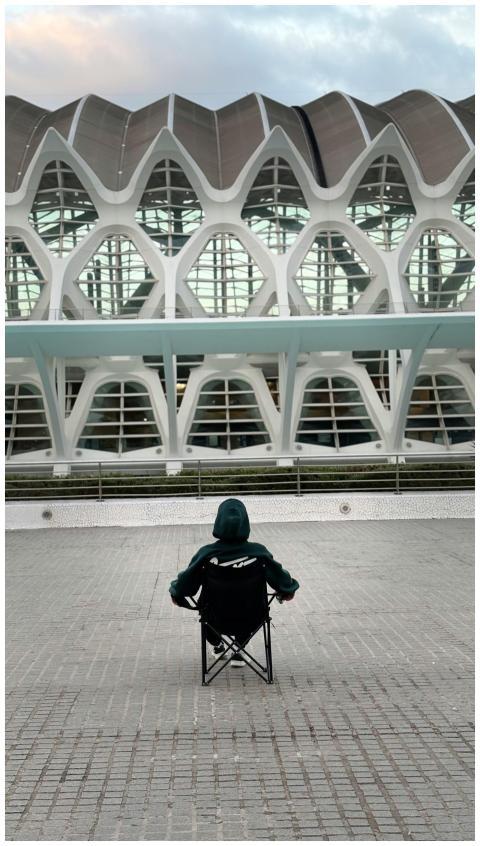 A person sits in front of a futuristic building, r