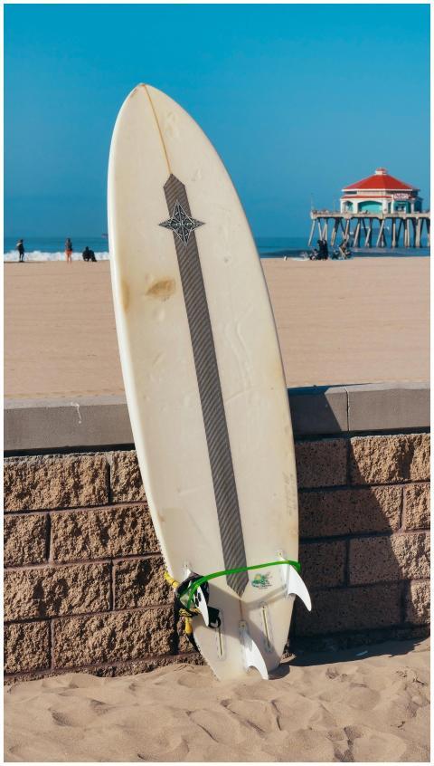 Surfboard against a sandy beach and pier backdrop,