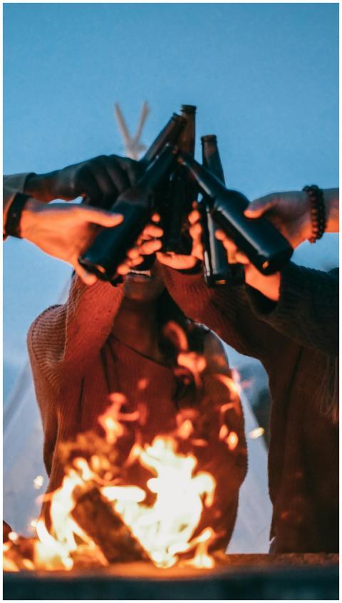 A group of friends enjoys a bonfire, toasting beer