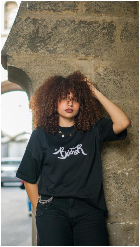 A young woman with curly hair poses confidently ag