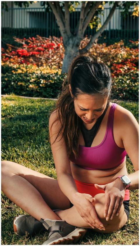 A young woman in activewear sitting on grass, mass