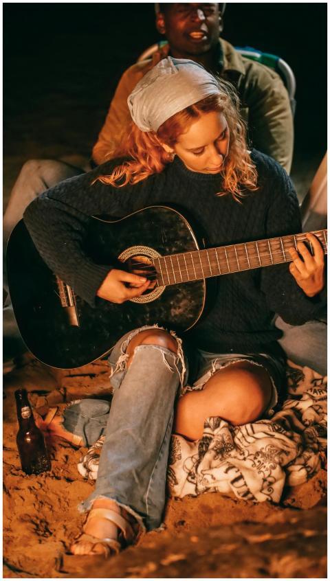 Young woman plays guitar around a beach bonfire wi