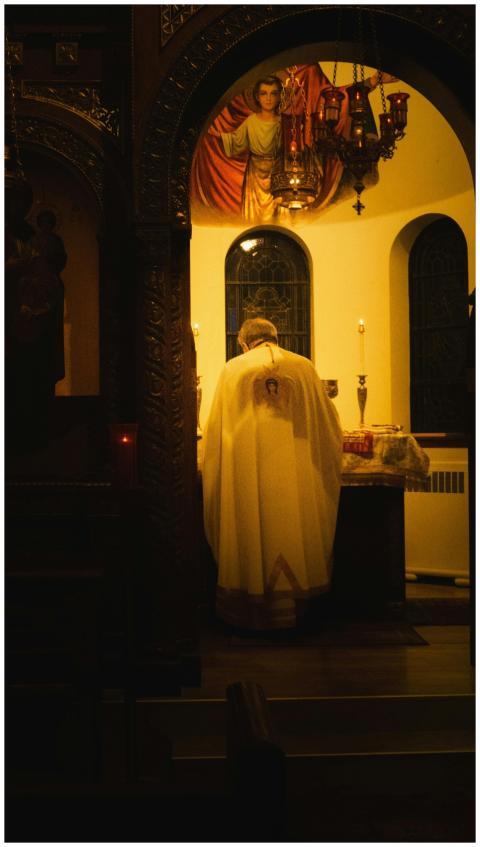 A priest in a white robe conducts a candlelit reli