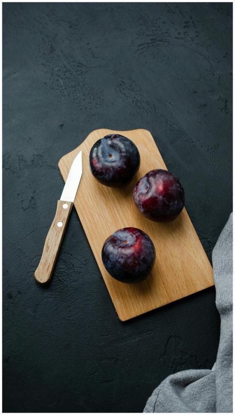 Three ripe plums on a wooden board with a knife on