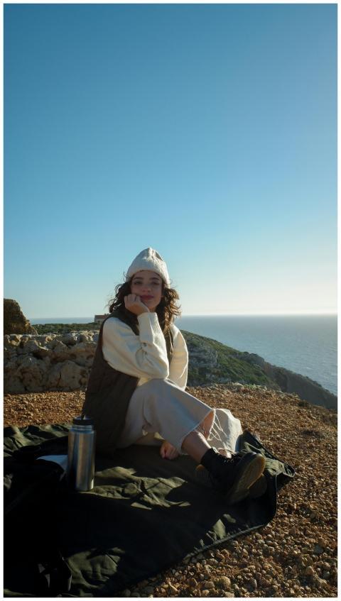 A woman enjoys a sunny day on a rocky cliffside, s