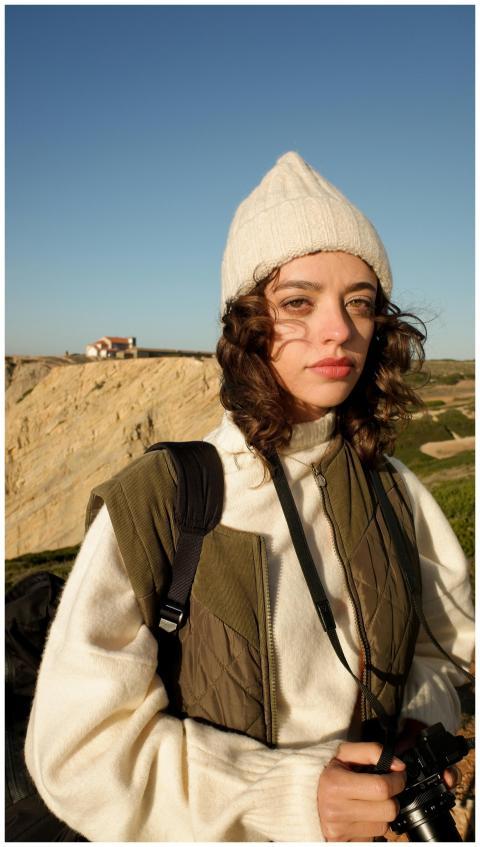 A young woman in a beanie and puffer vest holds a