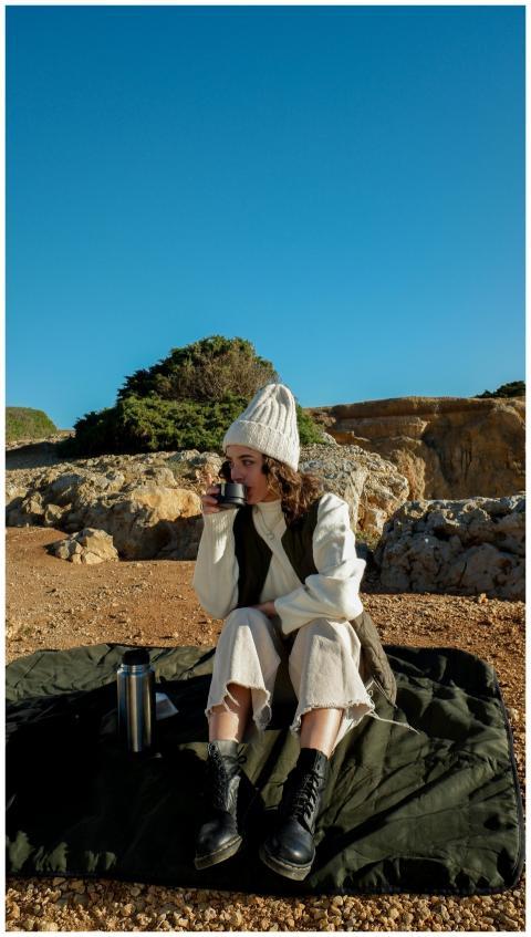 Woman in beanie drinking outdoors on a sunny day,