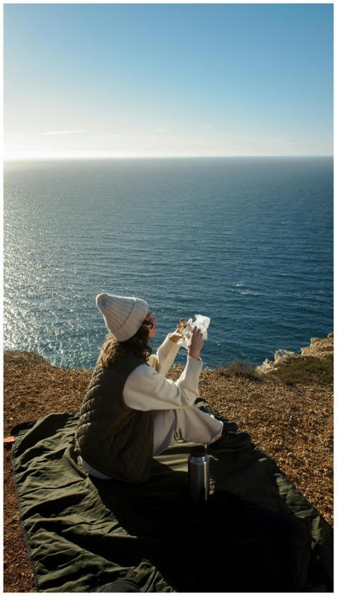 A woman in a beanie enjoys a view of the sea from