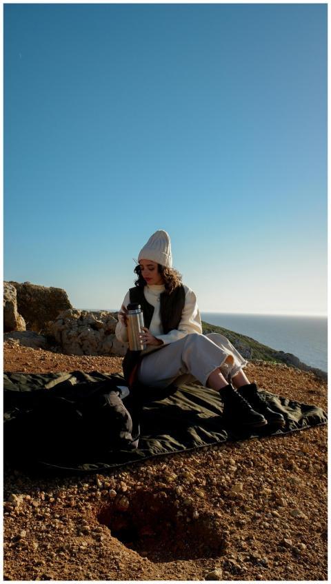 Woman with a knit hat sits outdoors enjoying a hot
