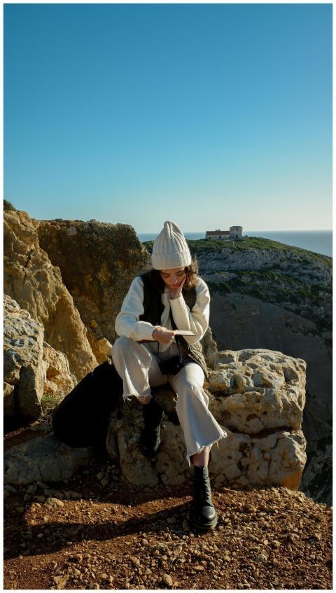 Woman in knit hat sitting on cliff edge in Sesimbr