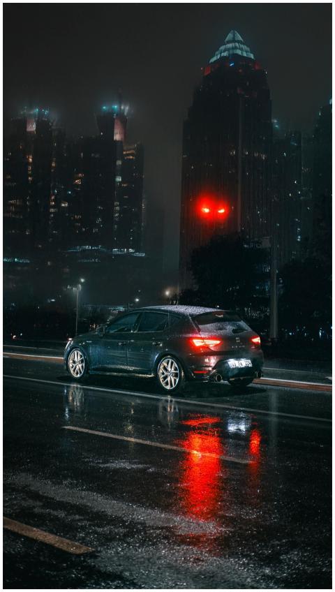 A sleek car on a wet city street reflecting tower