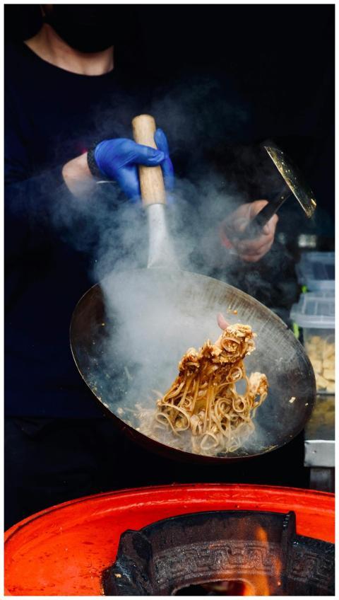 Chef cooking noodles in steaming wok, showcasing a