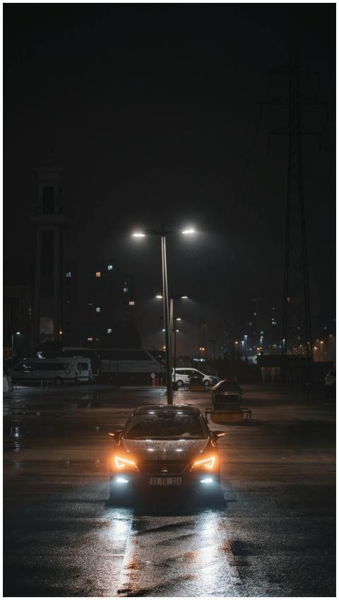 A sleek car with headlights on, parked under stree