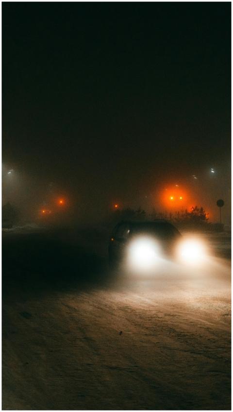 A car drives through snowy streets at night with g