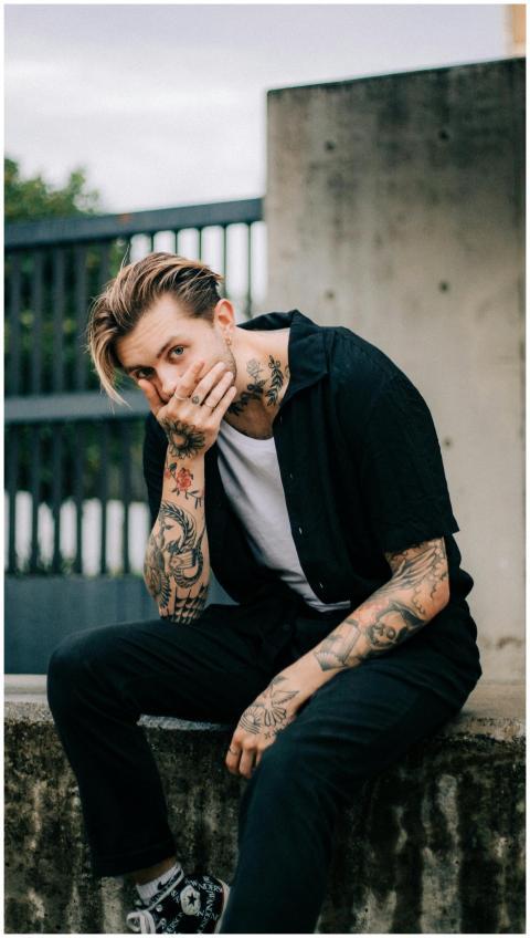Pensive tattooed man in casual wear sitting outsid