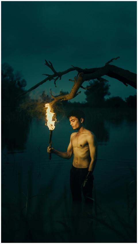 A shirtless man holds a torch at night by eerie wa