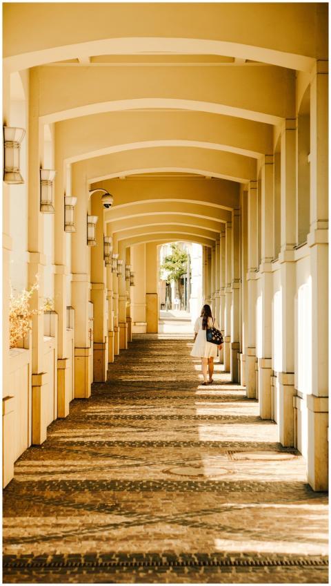 A woman walks through a sunlit, elegant arcade wal