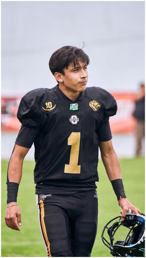 A young male football player in a black uniform ho