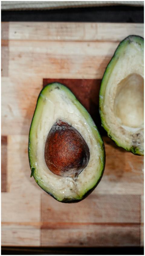 Fresh avocado sliced open on a wooden board, highl