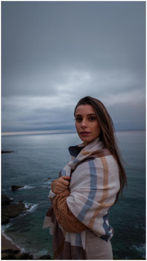 A woman stands wrapped in a blanket, gazing at the