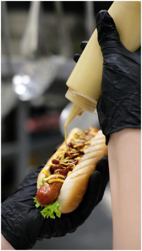 Delicious hot dog being topped with mustard and ke