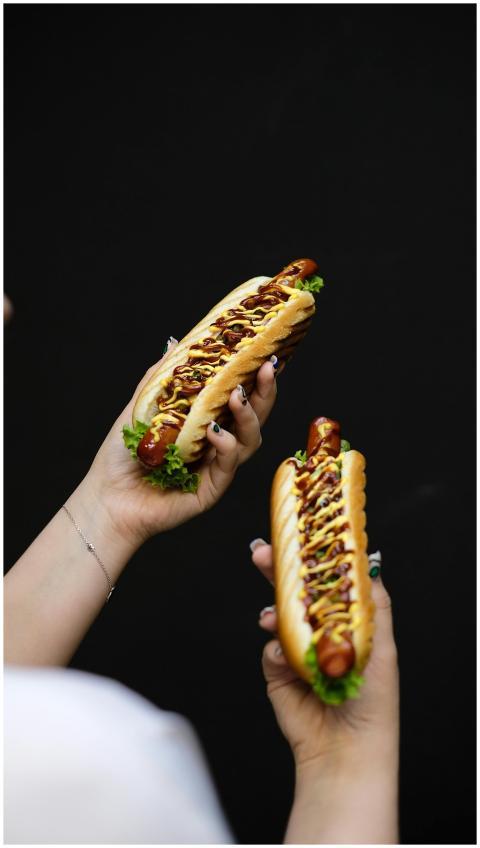 Two hot dogs held against a dark background with m
