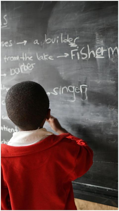 Young student in a red uniform writing on a blackb