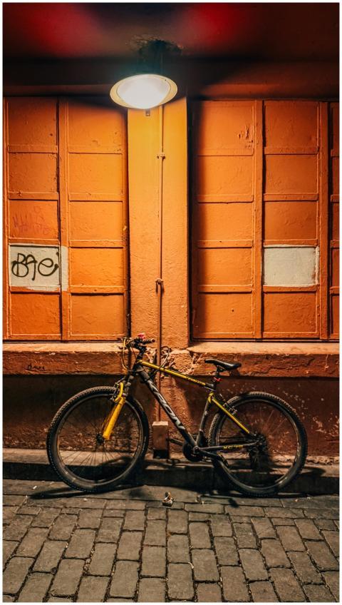 A bicycle leans against colorful wall under street