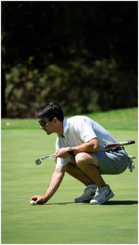A golfer crouches to position his ball on a sunlit