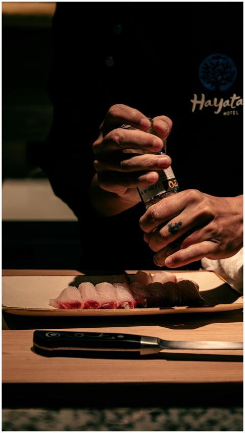 Chef sprinkling seasoning on sushi rolls in a diml