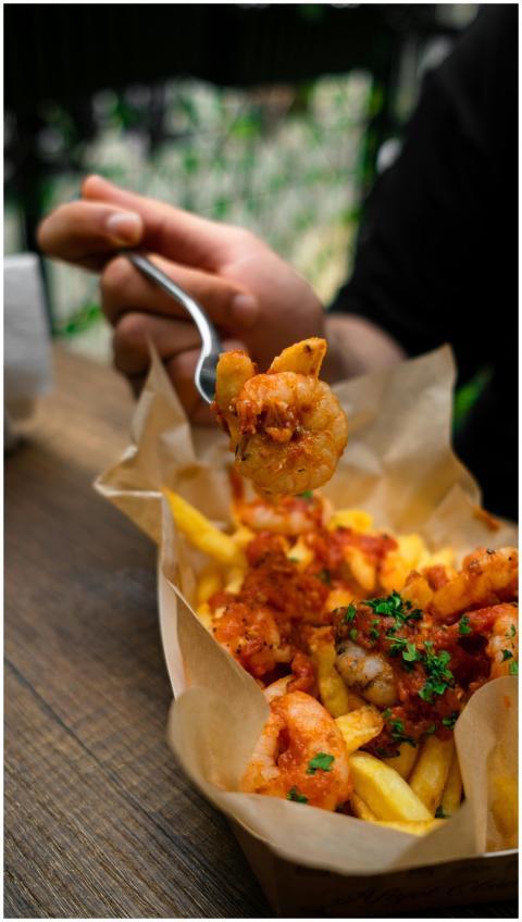 A hand holding a fork with shrimp over a basket of