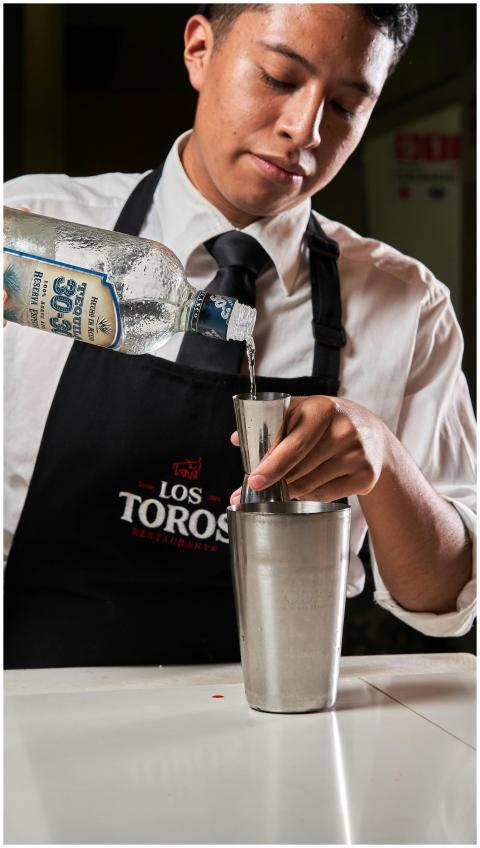 Young bartender precisely pouring tequila into a c