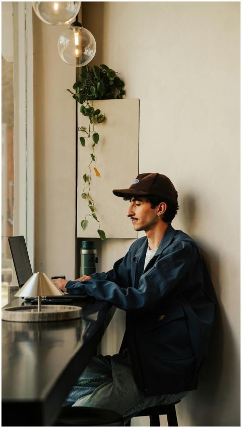 Young man wearing cap and jacket works on laptop i
