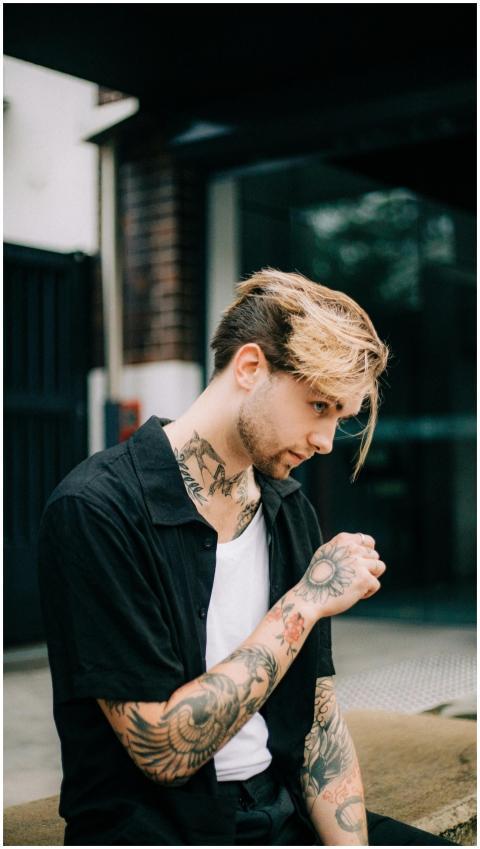 A young tattooed man sits pensively outdoors, show