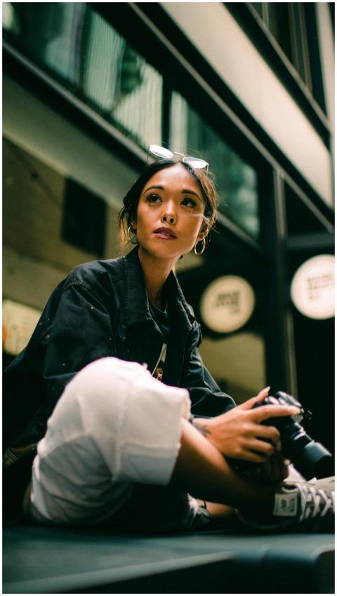 A fashionable woman sits indoors with a camera, ex
