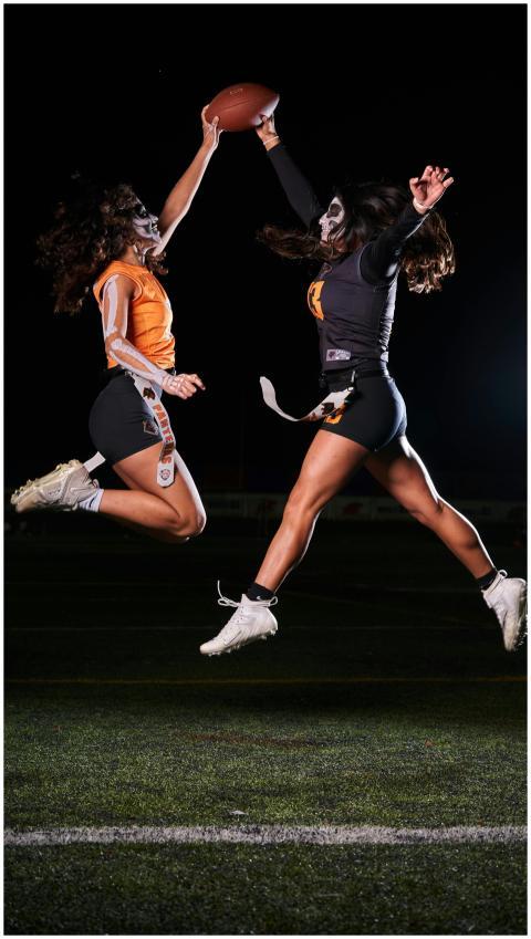 Two women in face paint leap for football at night