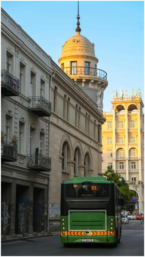 Green bus on a quiet city street lined with histor