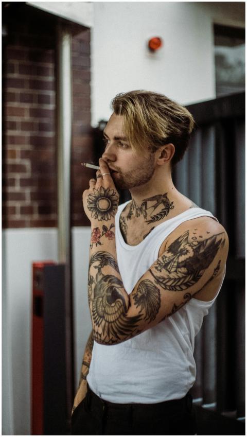 A portrait of a tattooed man smoking in an urban i