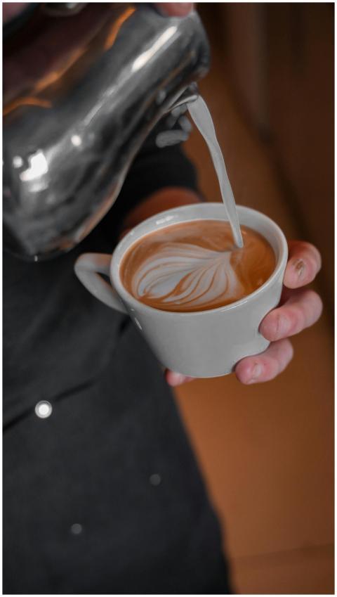 Close-up of hands pouring frothy milk into coffee