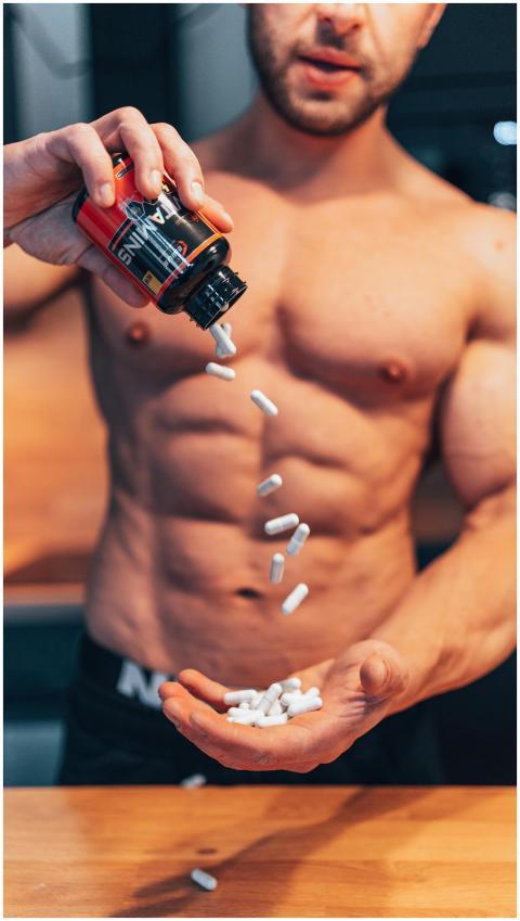 Shirtless man pouring white supplement capsules in