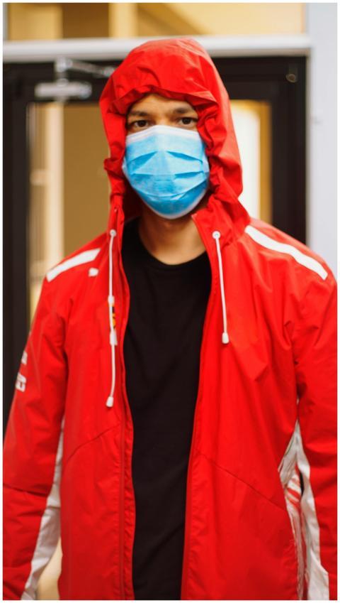 A person in a red jacket and face mask indoors, sy