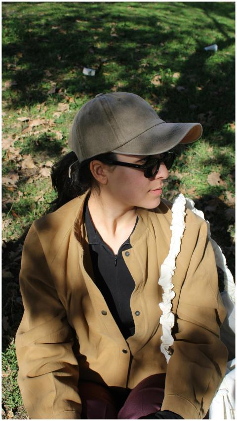 A woman with sunglasses and cap sits outside on a