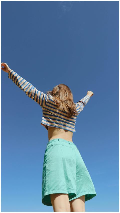 A young woman raises her arms in joy, wearing a st