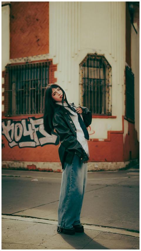 Trendy woman in black jacket posing against graffi